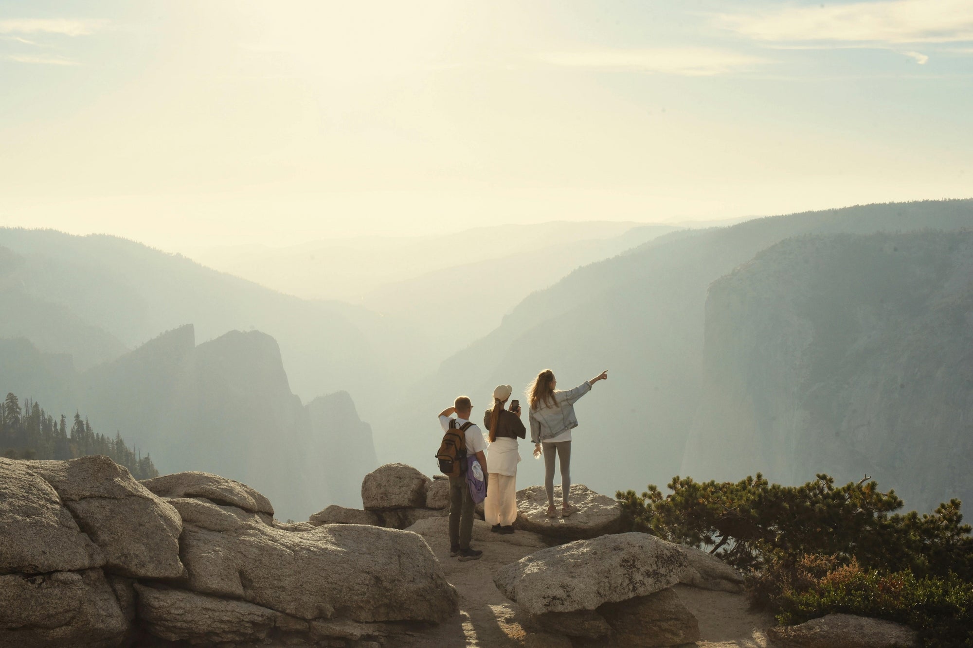 Four people standing on a rocky mountain ledge with a scenic view of mountains and sky.